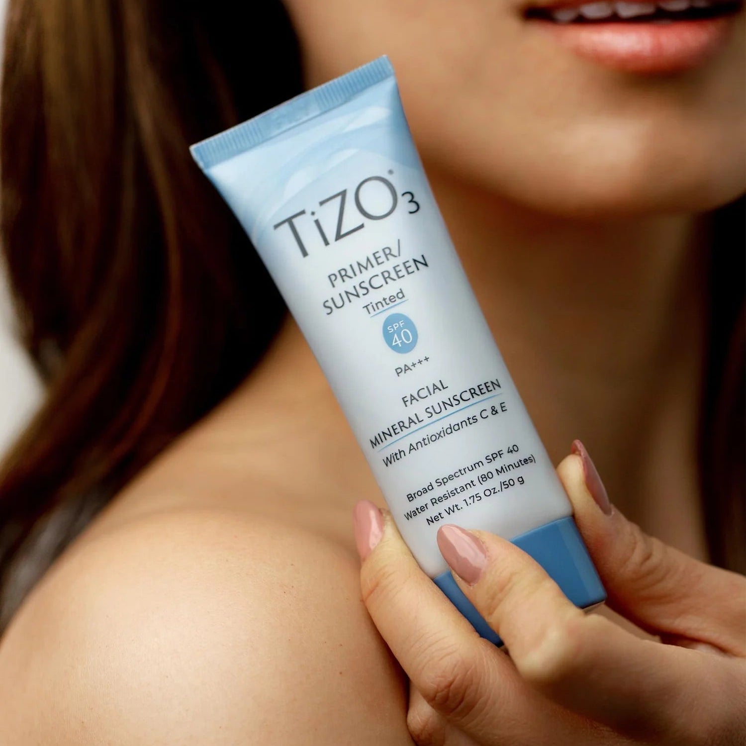 Person holding a TIZO3 sunscreen tube with a blurred background