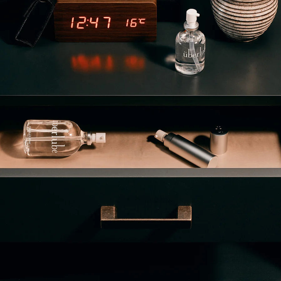 Dark wooden nightstand with open drawer displaying bottles and a clock on top.