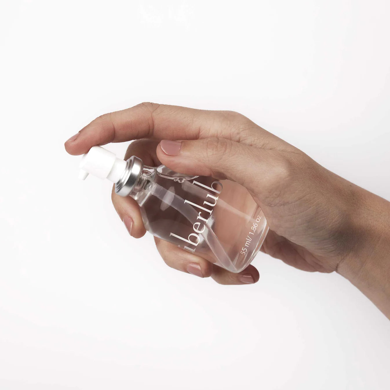 Hand holding UberLube Silicone Lubricant 55mL bottle from The Pharmacy Lab with clear glass packaging and pump dispenser.