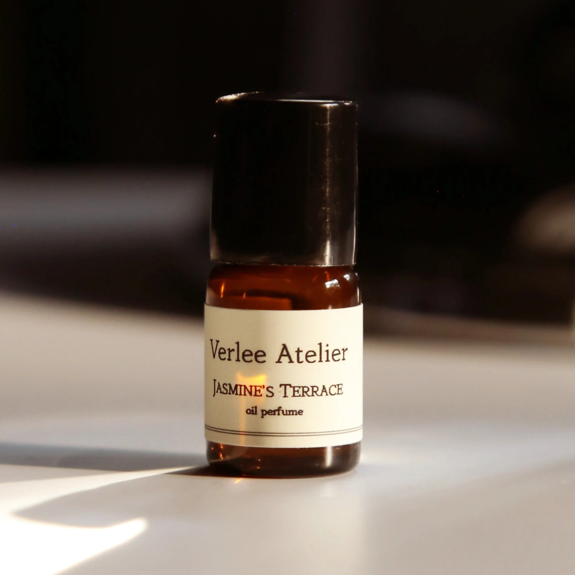 Bottle of Verlee Atelier Jasmine's Terrace oil perfume on a reflective surface with a dark background