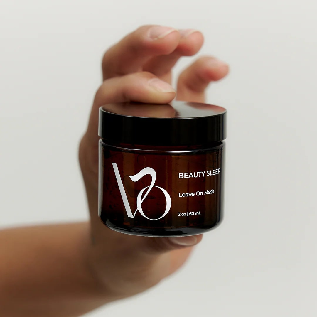 Hand holding a jar of 'VO Beauty Sleep Leave On Mask' against a plain background