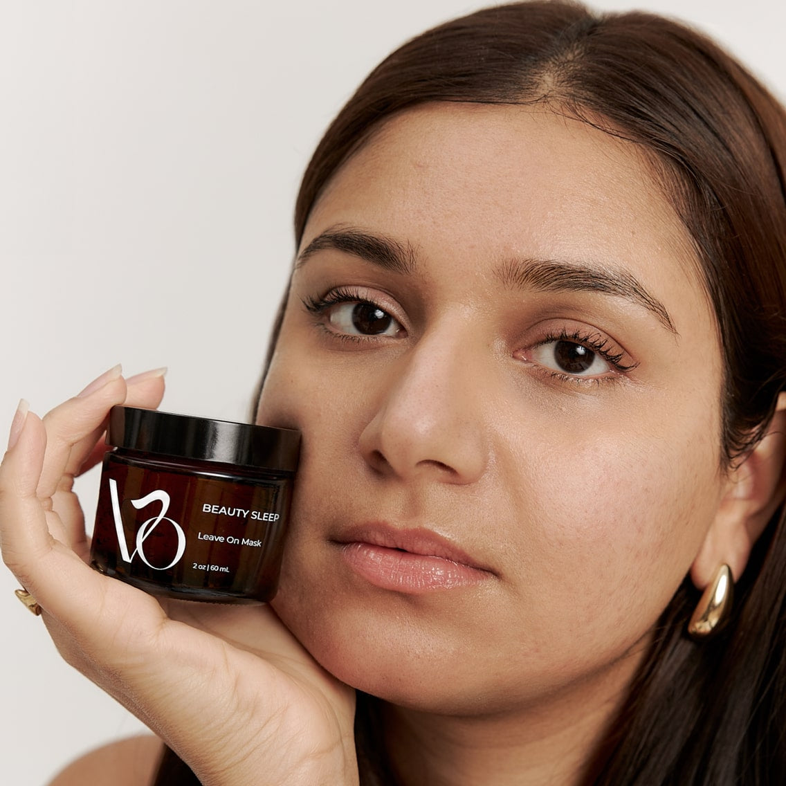 Woman holding a jar of VO Beauty product against a neutral background
