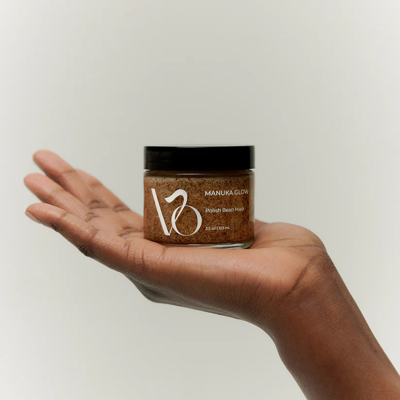 Hand holding a jar of Manuka Glow polish balm mask against a plain background