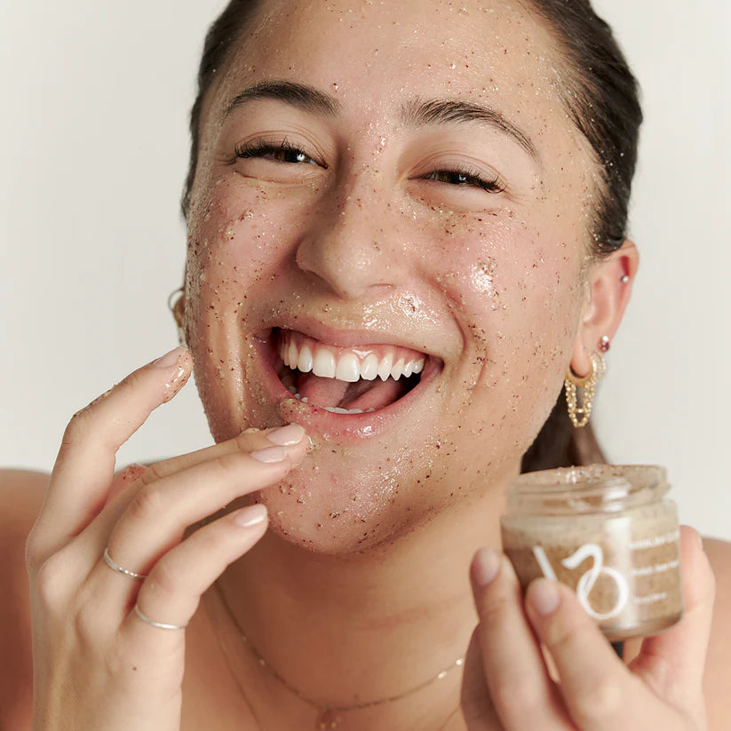 Person applying a facial scrub to their face with a jar labeled '100'.