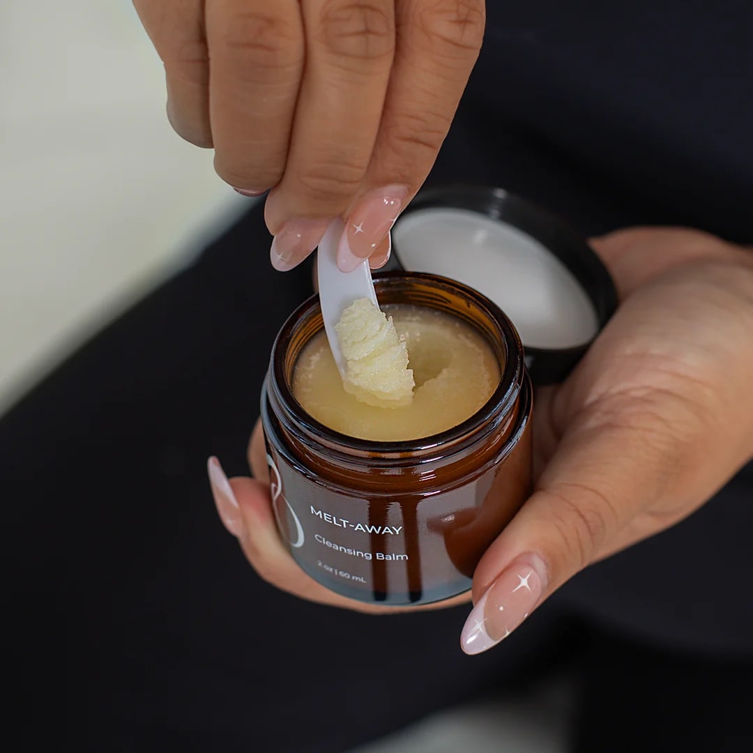 Person using a jar of 'Melt Away' cleansing balm with a applicator.