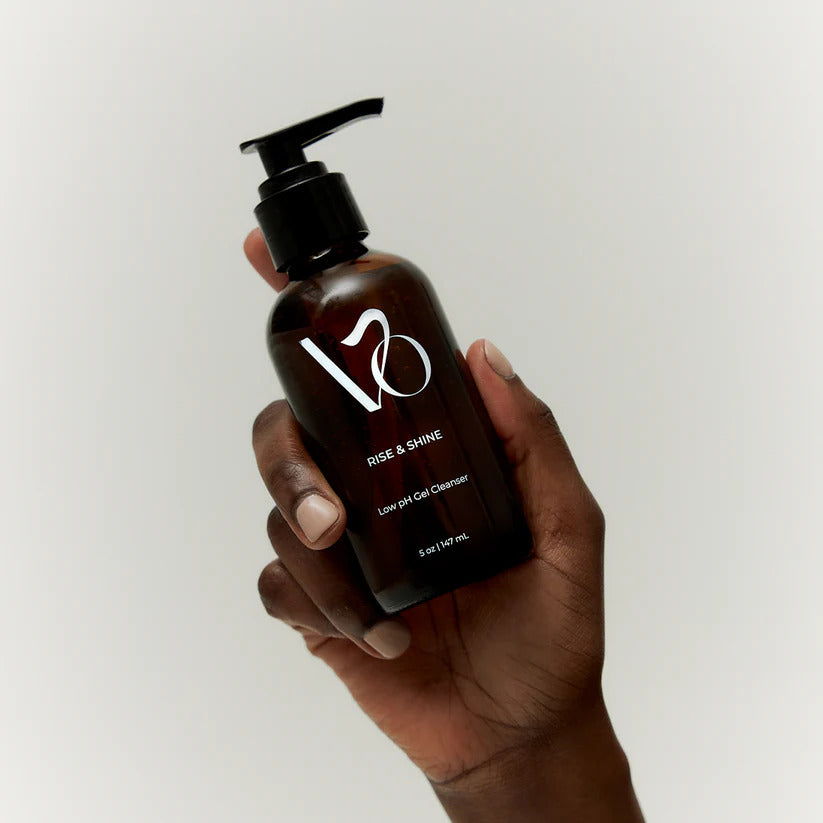 Hand holding a brown bottle labeled 'VO Rise & Shine' against a light background