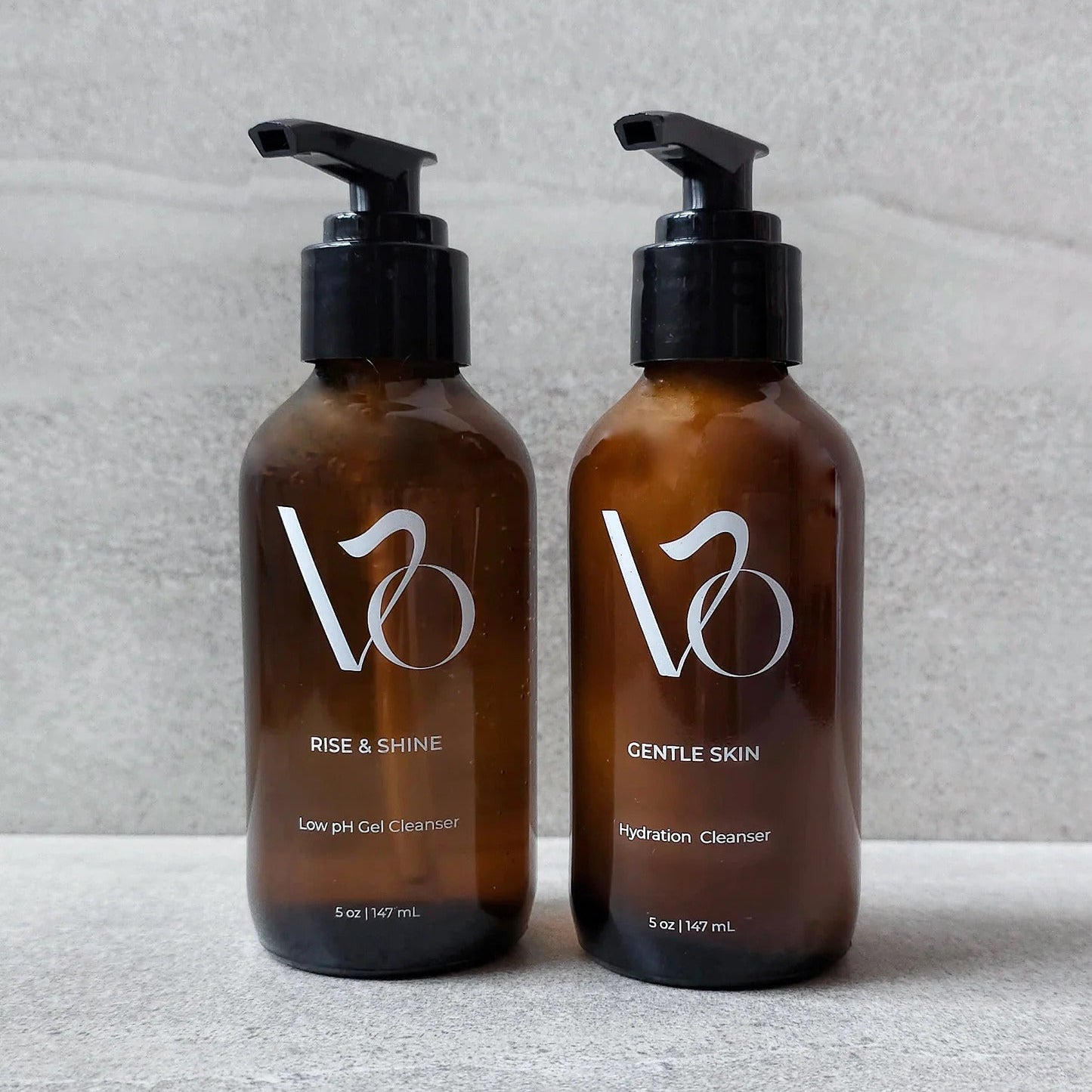 Two brown bottles with black pump dispensers on a light gray surface.