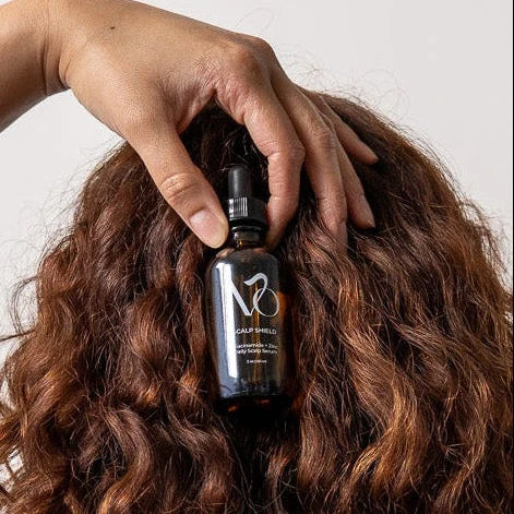 Hand holding a bottle labeled 'M8 Scalp Shield' over wavy hair