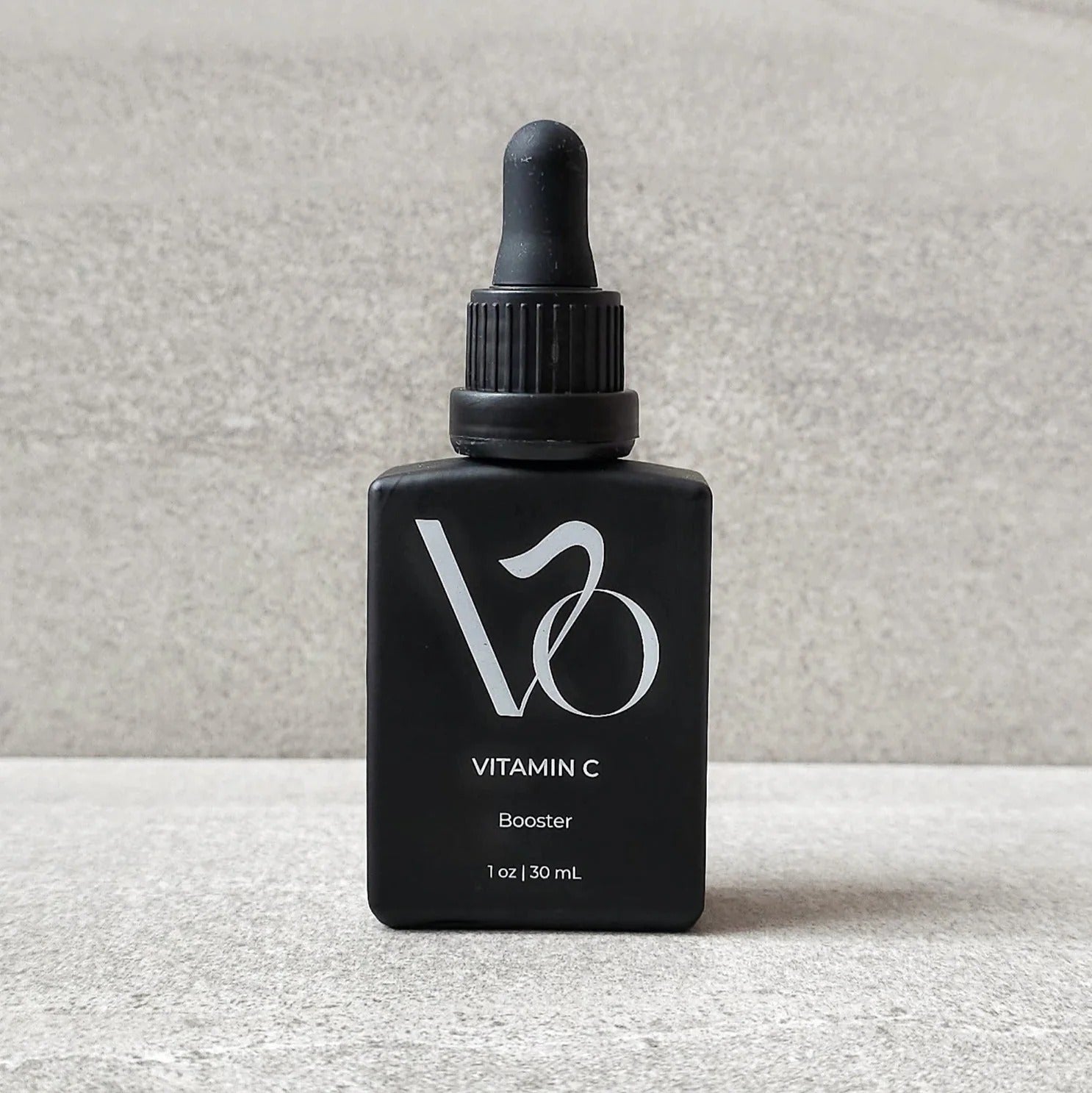 Black bottle with dropper labeled 'Vitamin C Booster' on a gray background