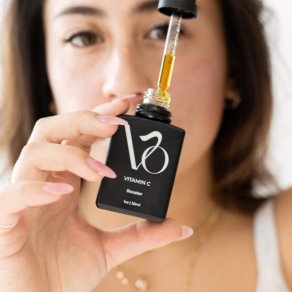 Woman holding a black bottle labeled 'Vitamin C Booster' with a dropper.